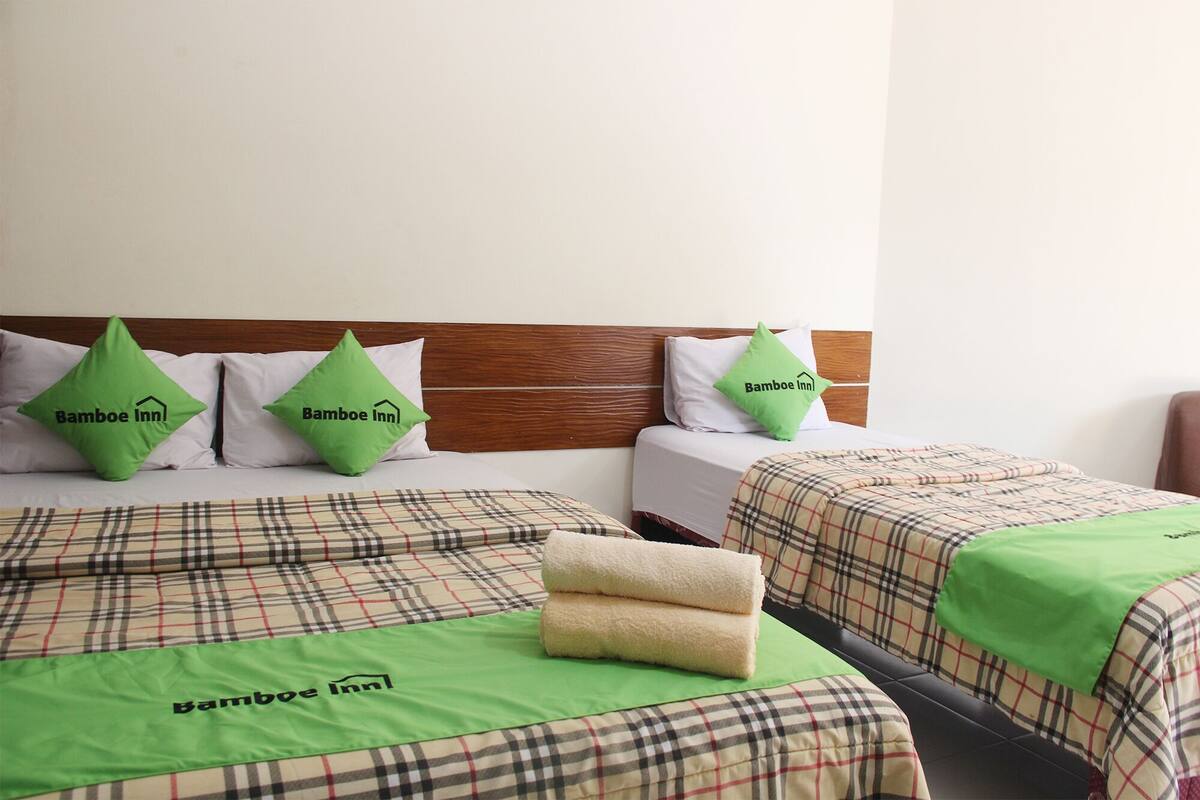Ett hotellrum med två sängar, var och en med ett rutigt överkast och gröna kuddar prydda med hotellets logotyp.