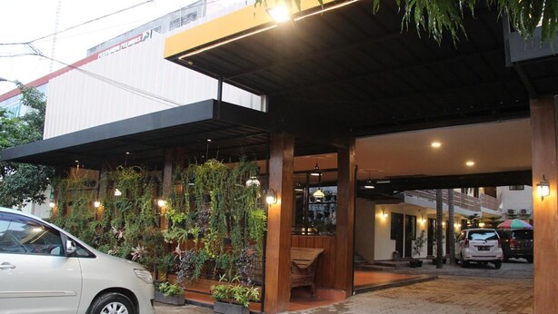 A building entrance with a covered outdoor seating area, a car parked in front, and a staircase leading to an upper level. - Bamboe Inn 2 Homestay (Bandar Lampung)