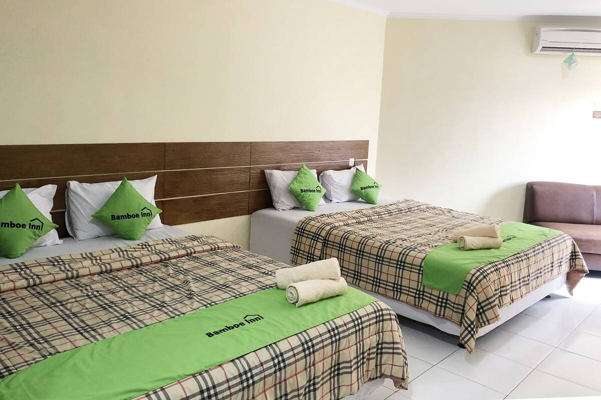 Ett hotellrum med två sängar, var och en med ett rutigt överkast och gröna kuddar, samt en brun sänggavel.