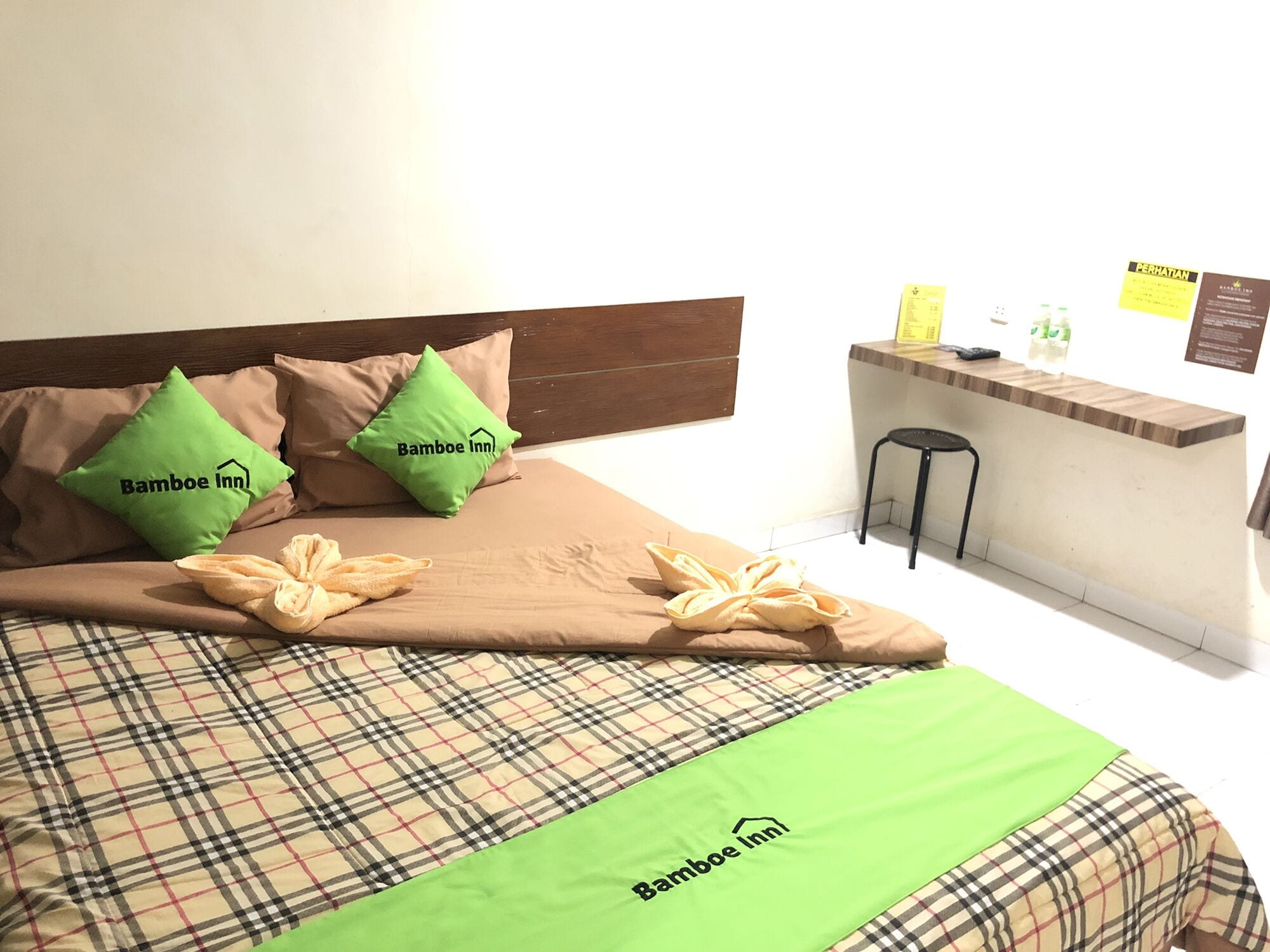 A bed with a plaid bedspread, two green pillows with "Bamboo Inn" logo, a green throw blanket, and a wooden headboard.