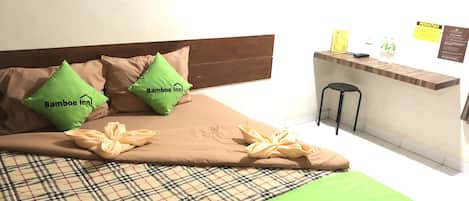 A bed with a plaid bedspread, two green pillows with "Bamboo Inn" logo, a green throw blanket, and a wooden headboard.