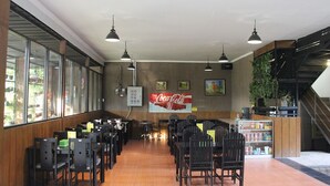 A restaurant with wooden paneling, black chairs, and a Coca-Cola poster on the wall. - Bamboe Inn 2 Homestay (Bandar Lampung)