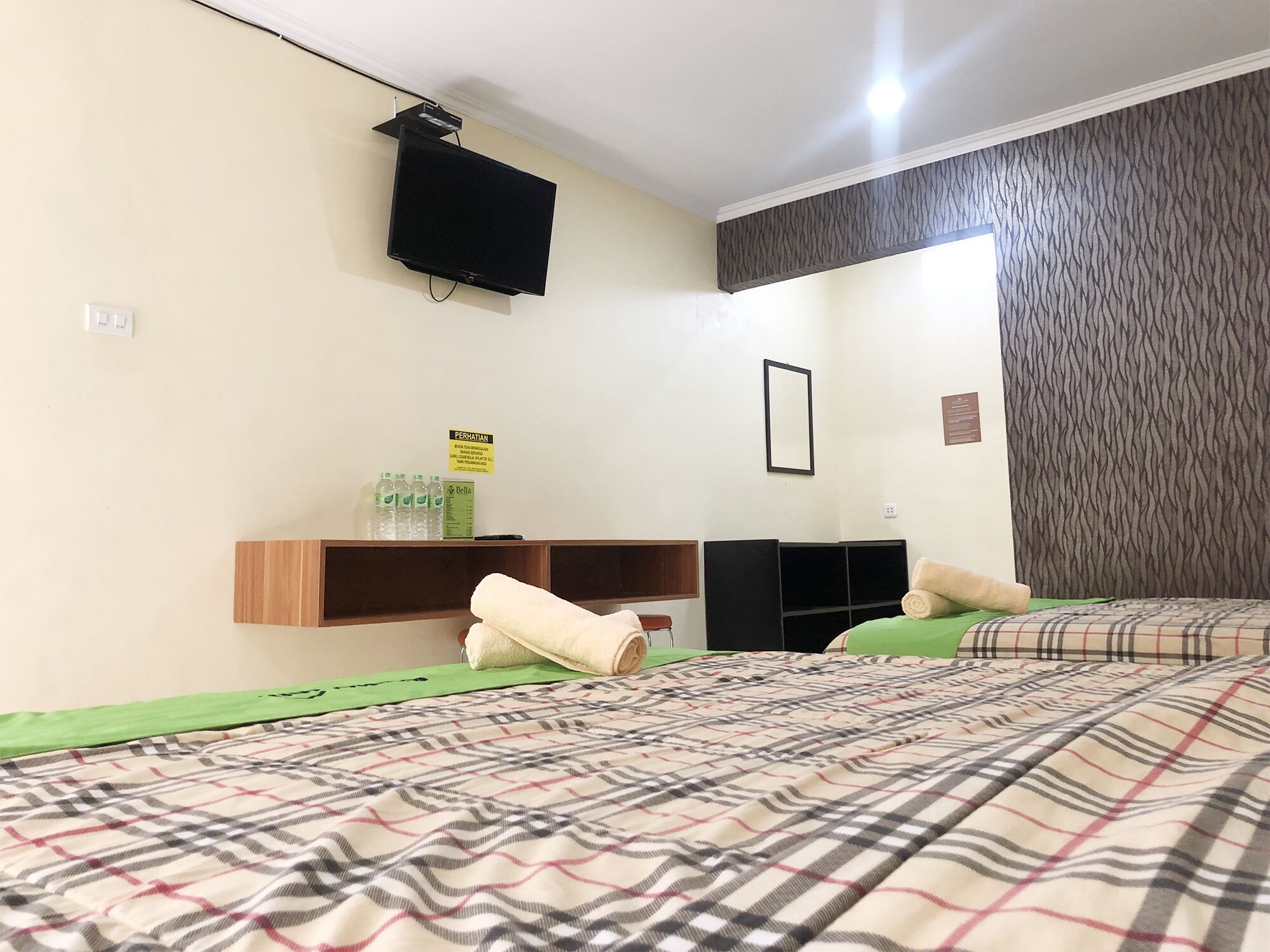 A hotel room with two beds, a flat-screen TV mounted on the wall, a shelf with toiletries, and a framed picture.