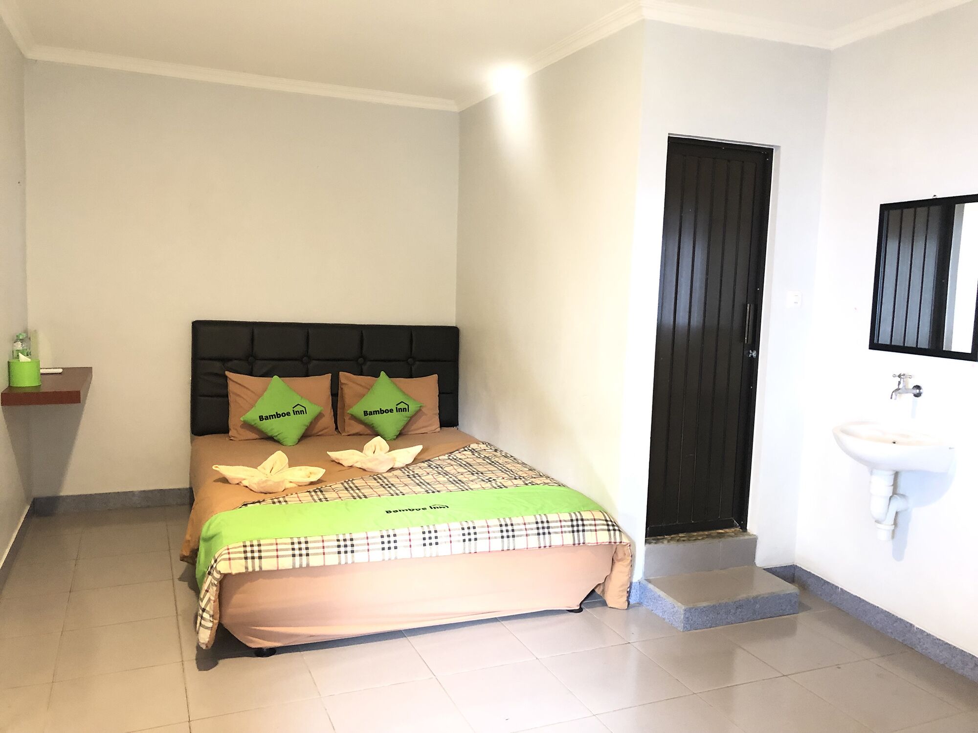 Une chambre à coucher comprenant un lit, des oreillers, une table de chevet, une porte et une salle de bain avec un lavabo.