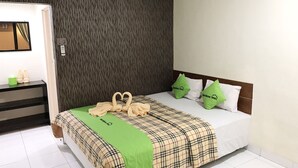 A hotel room with a bed, green pillows, a plaid bedspread, and a towel arrangement. - Bamboe Inn 2 Homestay (Bandar Lampung)