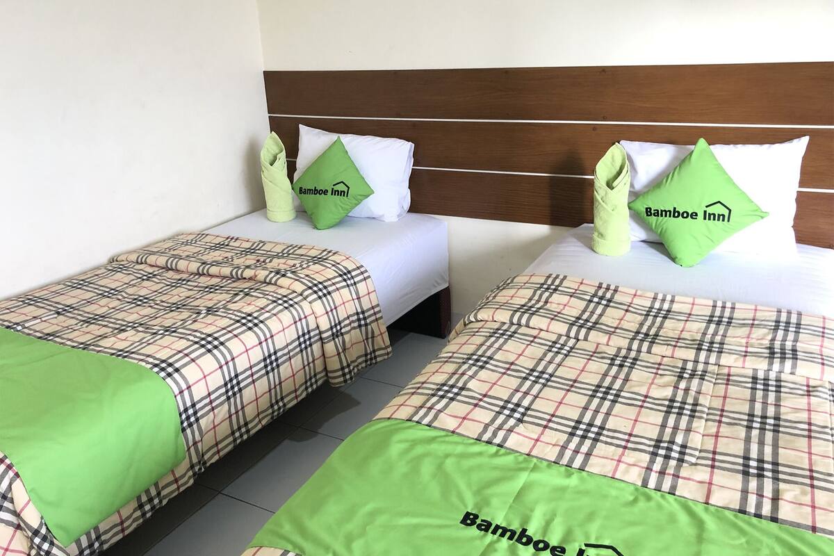 Två enkelsängar med rutigt sänglinne och gröna prydnadskuddar, var och en med logotypen för ”Bamboo Inn”.