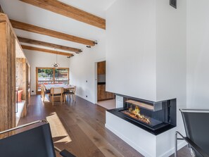 Una sala de estar moderna con chimenea, vigas de madera, un comedor y vistas al exterior.