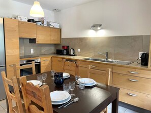 A modern kitchen with wooden cabinets, a built-in oven, a coffee maker, and a sink. - Central apartment in Chamonix with parking and wifi, near slopes (Chamonix-Mont-Blanc)
