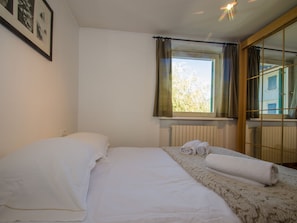 A bedroom with a bed, a window with curtains, a radiator, and a framed picture on the wall.