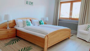 A bedroom with a wooden bed, two bedside tables with lamps, a radiator, and a window with curtains. - Vacation apartment Hochplatte 70 m², 1-4 persons, 1 sep. Bedroom, WLAN, Balcony (Unterwössen)