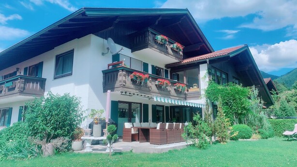 A two-story building with a balcony, outdoor seating, and a garden. - Vacation apartment Hochplatte 70 m², 1-4 persons, 1 sep. Bedroom, WLAN, Balcony (Unterwössen)