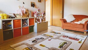 A cozy living room with a wooden ceiling, a plush orange sofa, a colorful train-themed rug, and a child's play area with toys and storage units. - Vacation apartment Hochplatte 70 m², 1-4 persons, 1 sep. Bedroom, WLAN, Balcony (Unterwössen)
