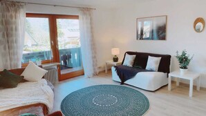 A bedroom with a bed, a sofa, a round rug, a nightstand, a lamp, a potted plant, and a window with curtains. - Vacation apartment Hochplatte 70 m², 1-4 persons, 1 sep. Bedroom, WLAN, Balcony (Unterwössen)