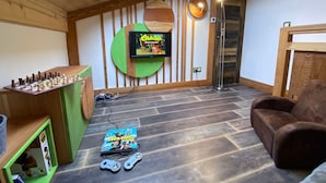 Una habitación acogedora con techo de madera, televisor montado, un tablero de ajedrez y una consola de videojuegos.