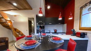 Un comedor con una mesa redonda dispuesta para seis personas, sillas rojas y una cocina moderna al fondo.