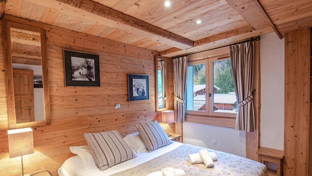 A wooden cabin bedroom with a bed, two pillows, a nightstand, a lamp, and two framed pictures on the wall. - Spacious apartment in Chamonix - Sleeps 6 - Wifi and parking (Chamonix-Mont-Blanc)