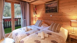 A wooden cabin room with two beds, a painting, and a balcony with curtains. - Spacious apartment in Chamonix - Sleeps 6 - Wifi and parking (Chamonix-Mont-Blanc)