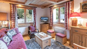 A cozy room with wooden beams, a sofa with patterned cushions, a television, and a red lamp. - Spacious apartment in Chamonix - Sleeps 6 - Wifi and parking (Chamonix-Mont-Blanc)