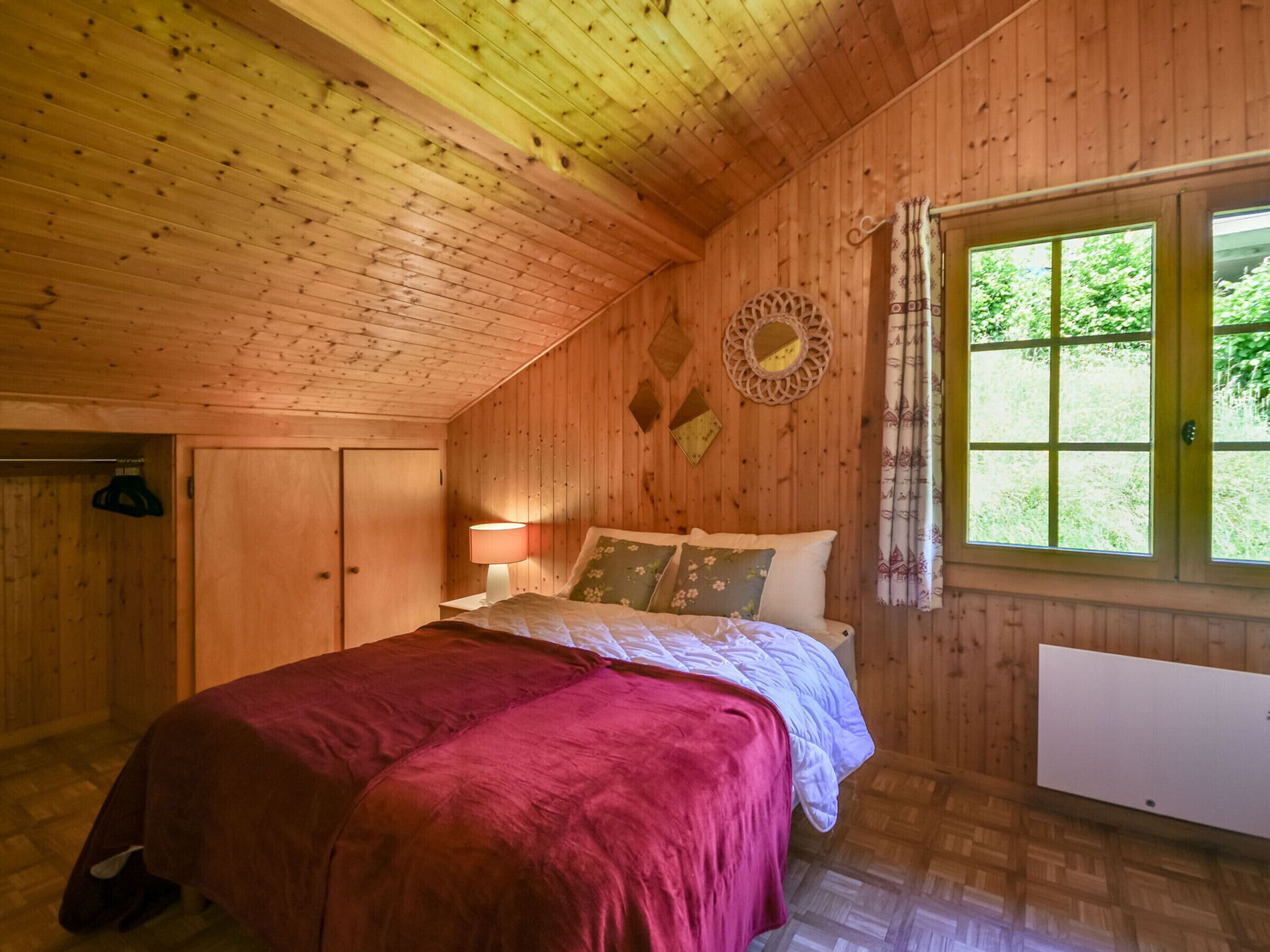 Um quarto de madeira com uma cama, uma janela e um espelho na parede.