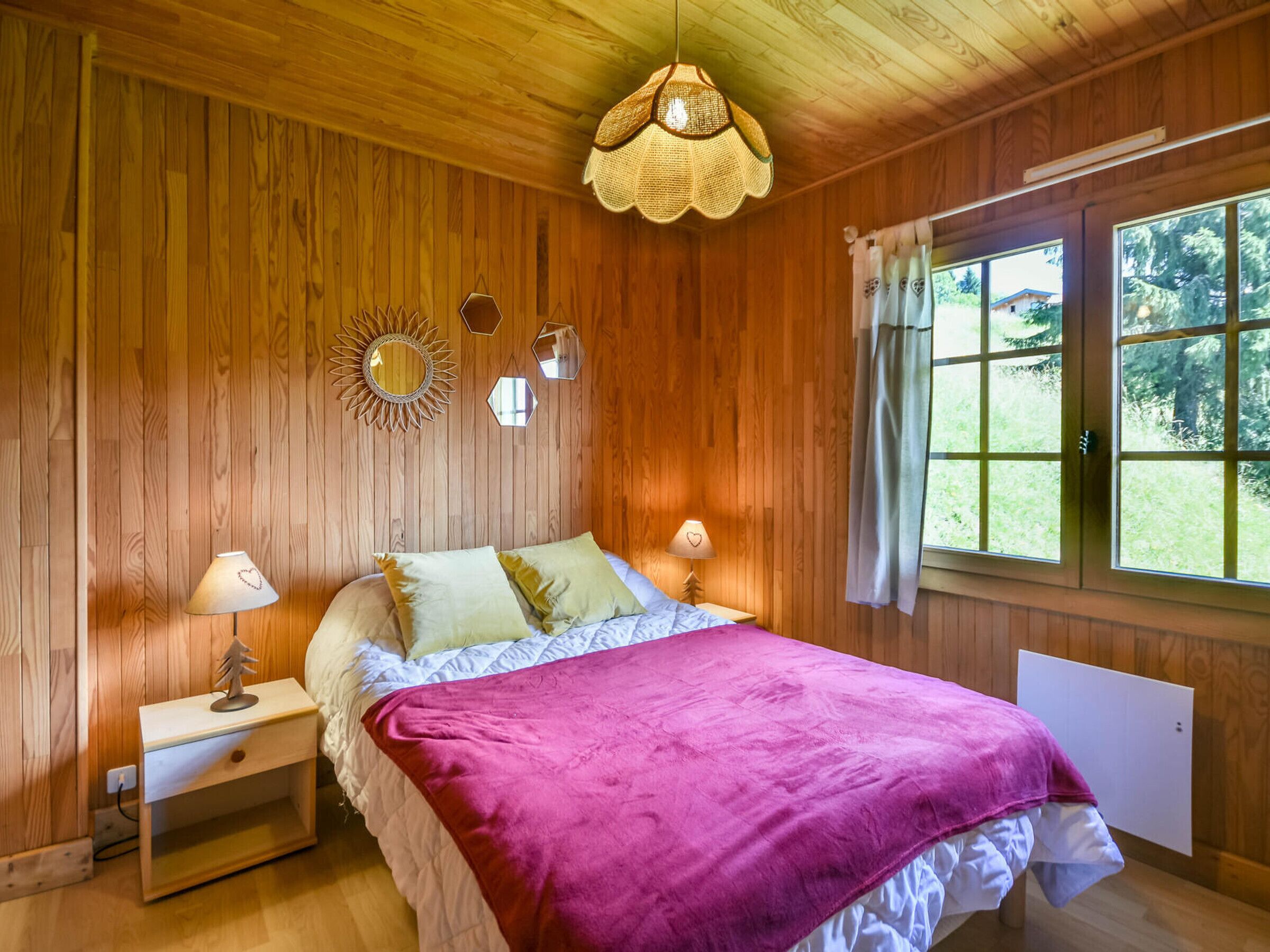 A wooden-paneled bedroom with a bed, two bedside tables, a hanging light fixture, and a window with curtains.