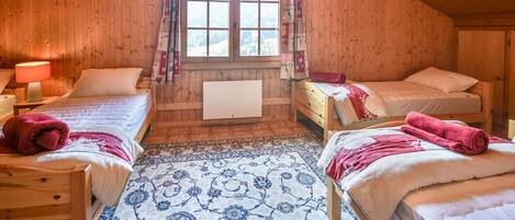 Un dormitorio abrigado en el ático, con dos camas, una ventana con cortinas y techo de madera.