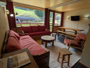 A cozy room with a sofa, a round table, and a wooden bench. - Large South Apt · Ski-in/out · Balcony · 8 pers. (La Plagne)