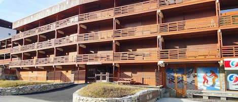 A multi-story wooden building with balconies, a stone wall, and a ski resort sign.