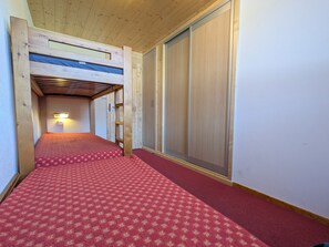 A narrow hallway with a red carpet leading to a room with a bunk bed. - Large South Apt · Ski-in/out · Balcony · 8 pers. (La Plagne)
