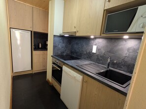 A compact kitchen with wooden cabinets, a built-in microwave, and a dishwasher.