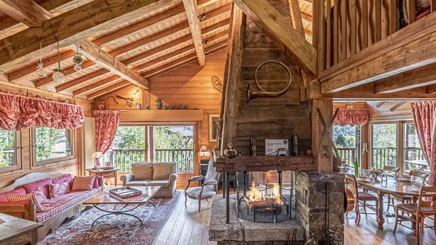 A cozy cabin interior with a stone fireplace, wooden beams, and a balcony with outdoor seating. - Typical Chalet in Chamonix with Parking and Wifi, Near Center and Slopes (Chamonix-Mont-Blanc)