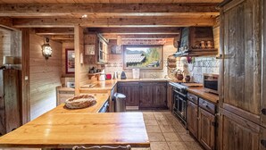 A rustic kitchen with wooden cabinets, a large wooden table, and a view of the outdoors through a window. - Typical Chalet in Chamonix with Parking and Wifi, Near Center and Slopes (Chamonix-Mont-Blanc)