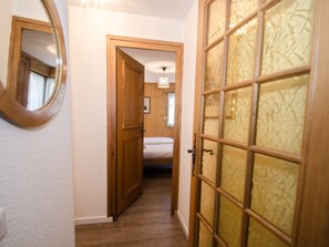 A hallway with a wooden door, a mirror, and a bed in the background.