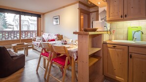 A cozy kitchen with wooden cabinets, a dining area with a table and chairs, and a view through large windows. - Lovely apartment in Chamonix center, near slopes with parking (Chamonix-Mont-Blanc)