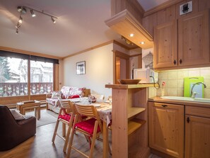 Une cuisine chaleureuse avec des meubles en bois, un coin repas avec une table et des chaises, et une vue magnifique grâce à de grandes fenêtres.