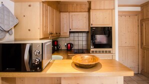A kitchen with wooden cabinets, a microwave, a stove, and a wooden bowl on the counter. - Lovely apartment in Chamonix center, near slopes with parking (Chamonix-Mont-Blanc)