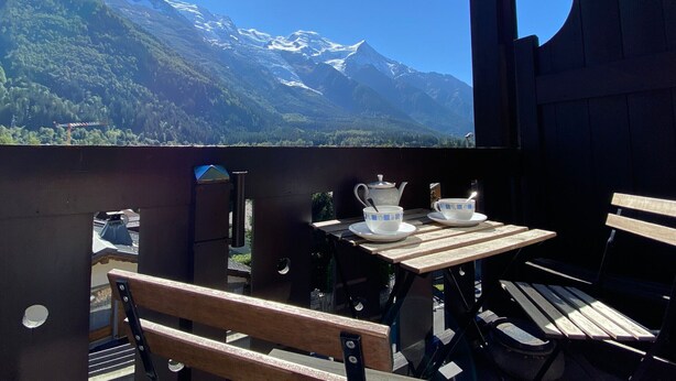 Une terrasse en bois avec une table et des chaises, offrant une vue sur un paysage montagneux aux sommets enneigés.