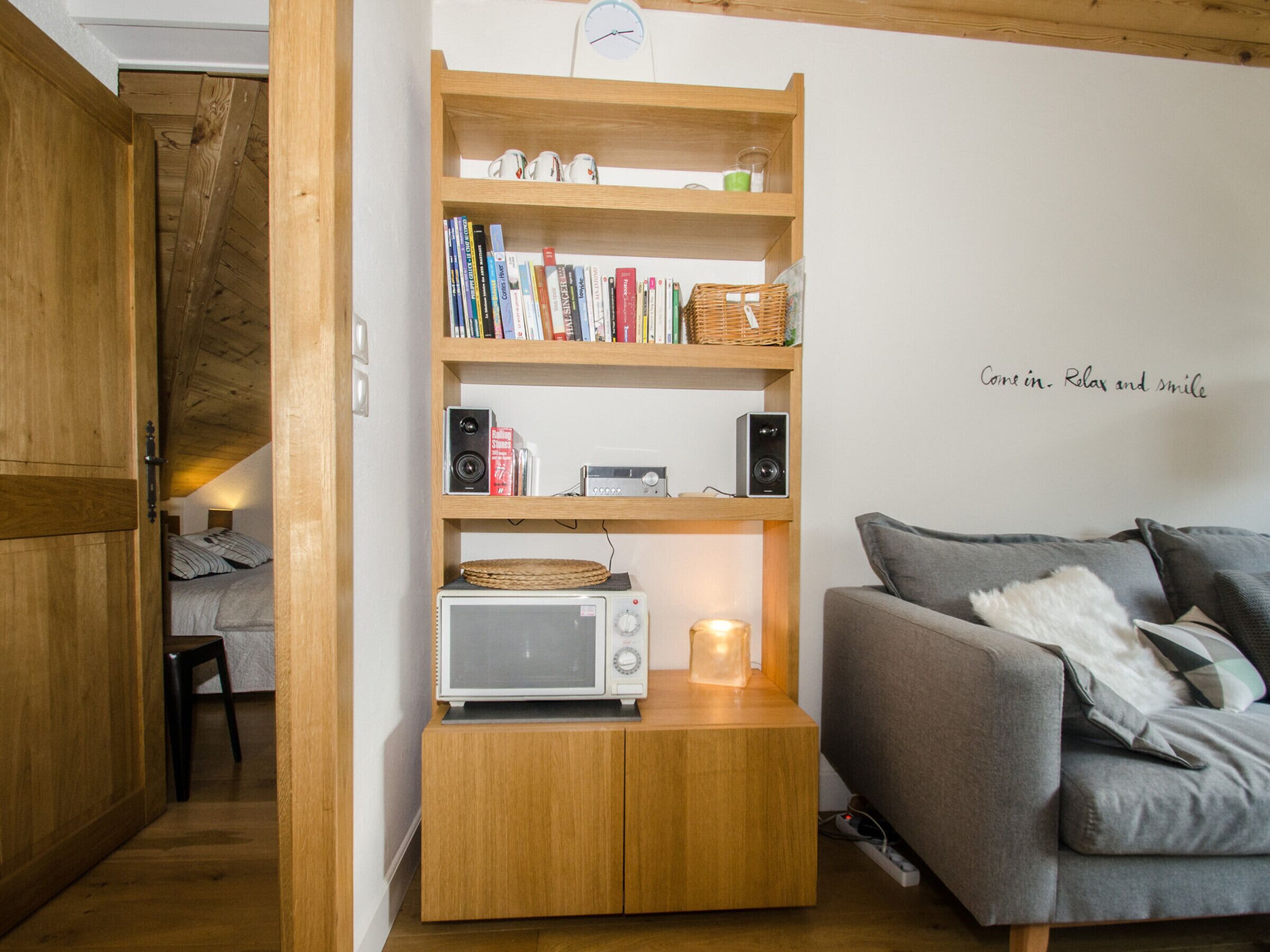 A cozy room with a wooden bookshelf, a grey sofa, and a small table with a microwave.