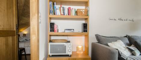 A cozy room with a wooden bookshelf, a grey sofa, and a small table with a microwave.