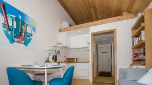 Une cuisine moderne avec des meubles blancs, une table à manger accompagnée de deux chaises bleues et un plafond en bois.