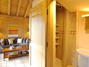 Een houten interieur met een bank, salontafel en een douchegedeelte met betegelde wanden.