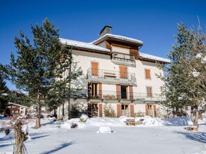Un immeuble à plusieurs étages, dont le toit est recouvert de neige, avec des balcons, et un ciel d’un bleu limpide.