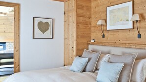 Een slaapkamer met een houten plafond, een bed met meerdere kussens, een hartvormig schilderij in een lijst en twee wandlampen.