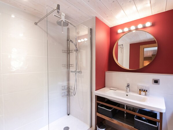 A modern bathroom with a glass-enclosed shower, a white sink with a mirror above it, and a red accent wall.