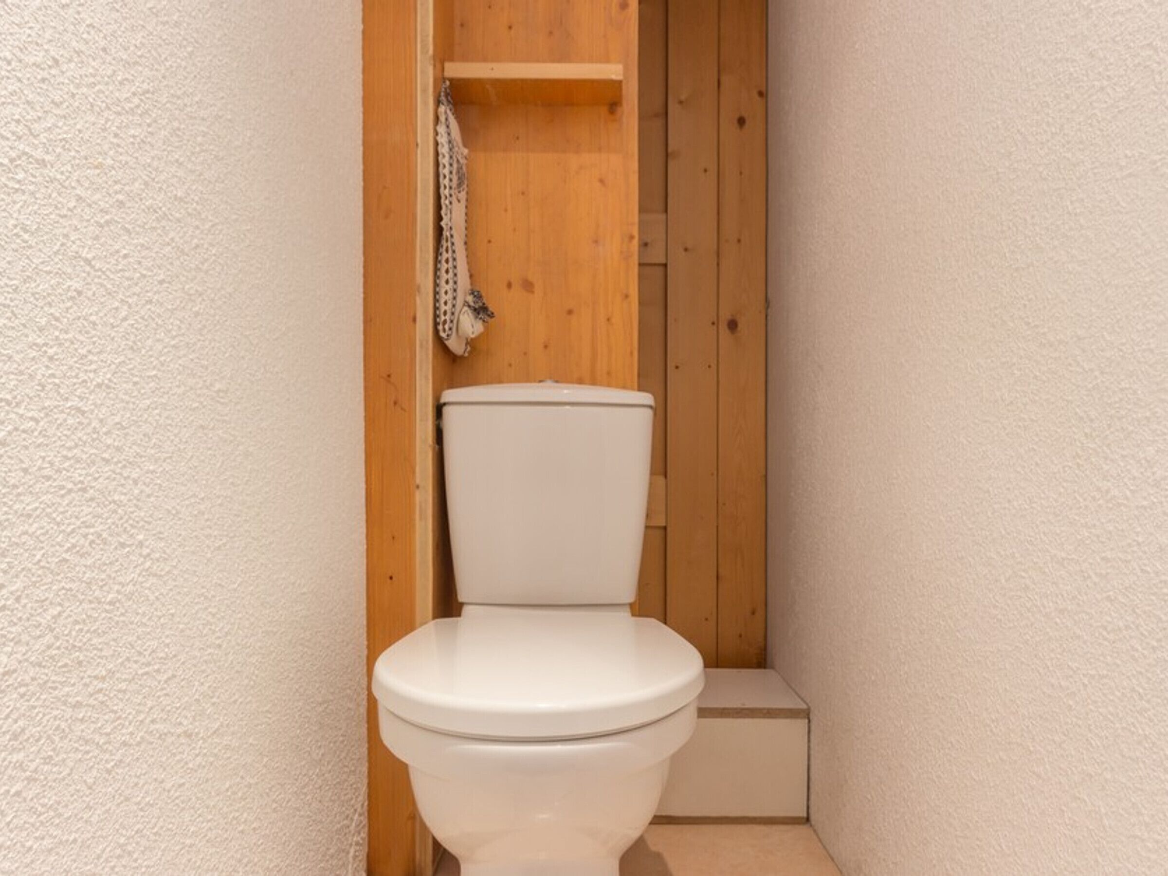 Ein kleines, kompaktes Badezimmer mit einer weißen Toilette, Holzwänden und einem Holzregal darüber.