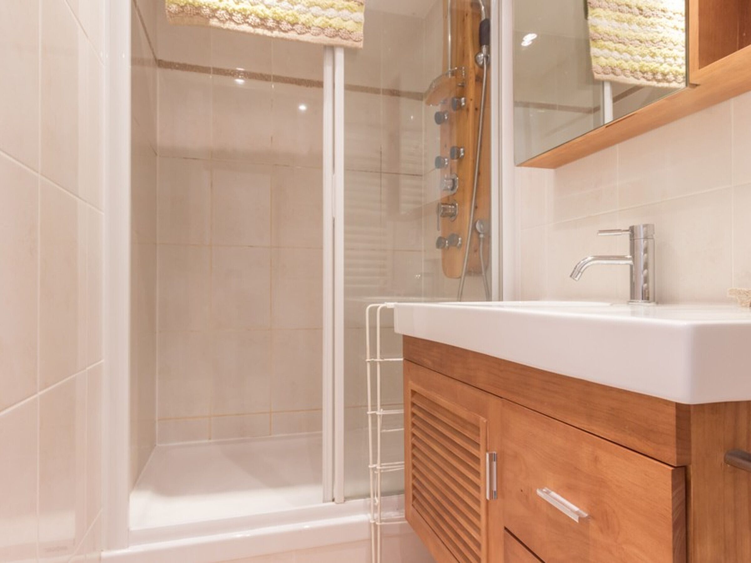 Un bagno moderno con doccia vetrata, mobile lavabo in legno e specchio sopra il mobile.