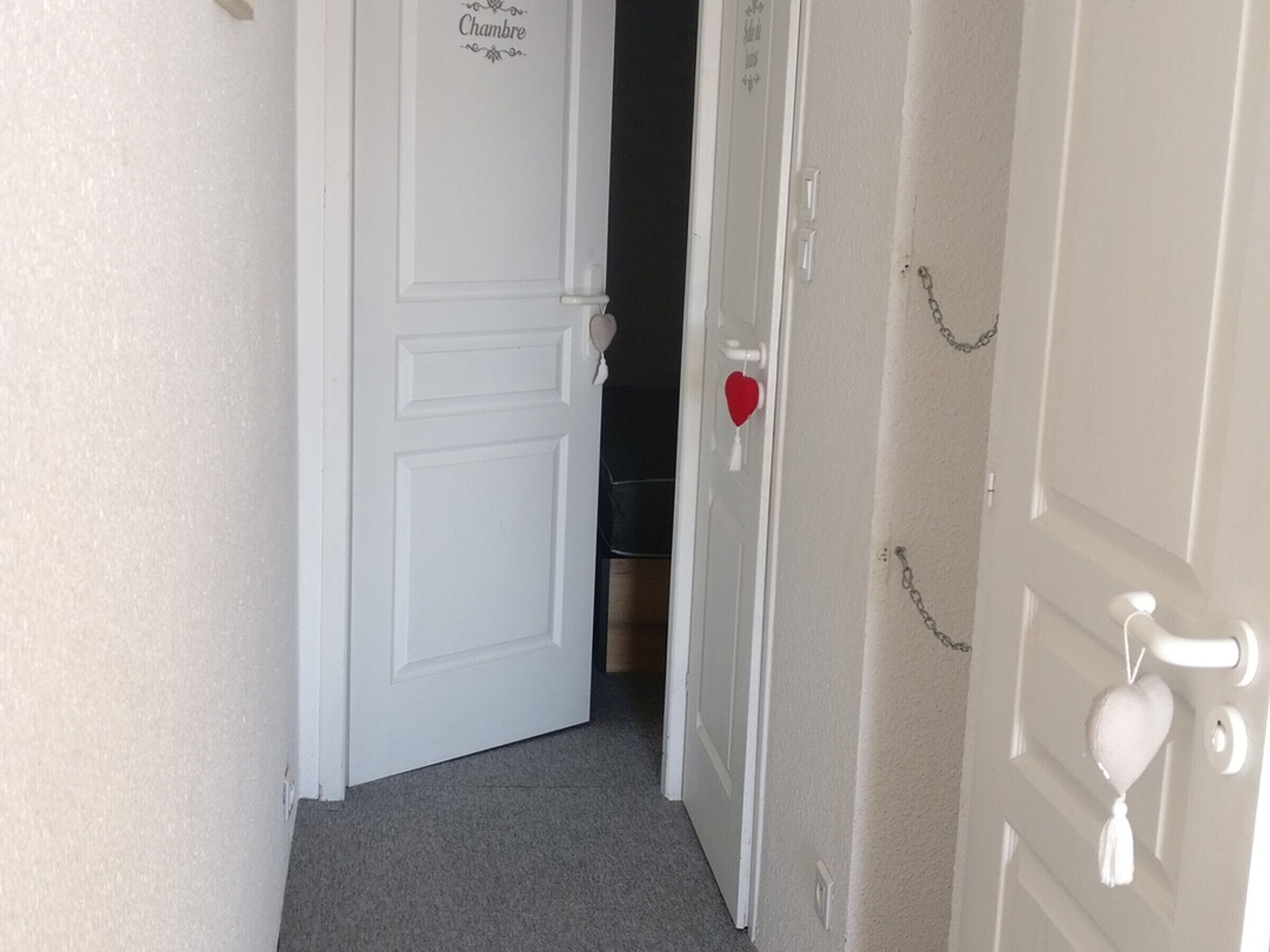 Un pasillo con una puerta blanca que dice 'Chambre' y una decoración con forma de corazón en otra puerta.