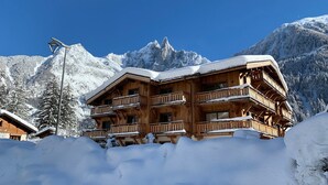 A wooden chalet with multiple balconies, surrounded by snow-covered mountains.