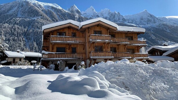 A wooden chalet with multiple balconies, surrounded by snow-covered mountains.