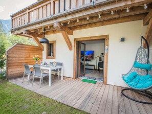 A wooden deck with a dining table and chairs, a hanging chair, and a television in a room.