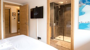 A hotel room with a bed, a shower, a mounted TV, and a framed picture on the wall.
